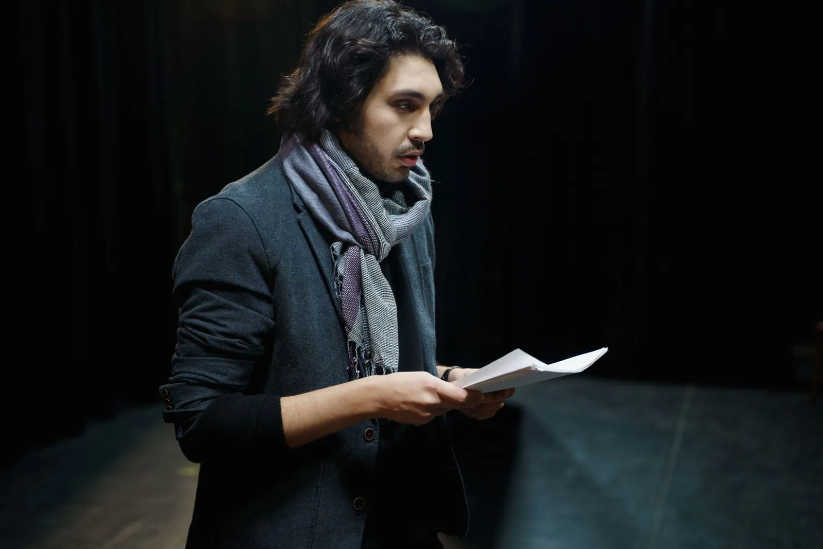 Actor ensayando un texto en un escenario en penumbra